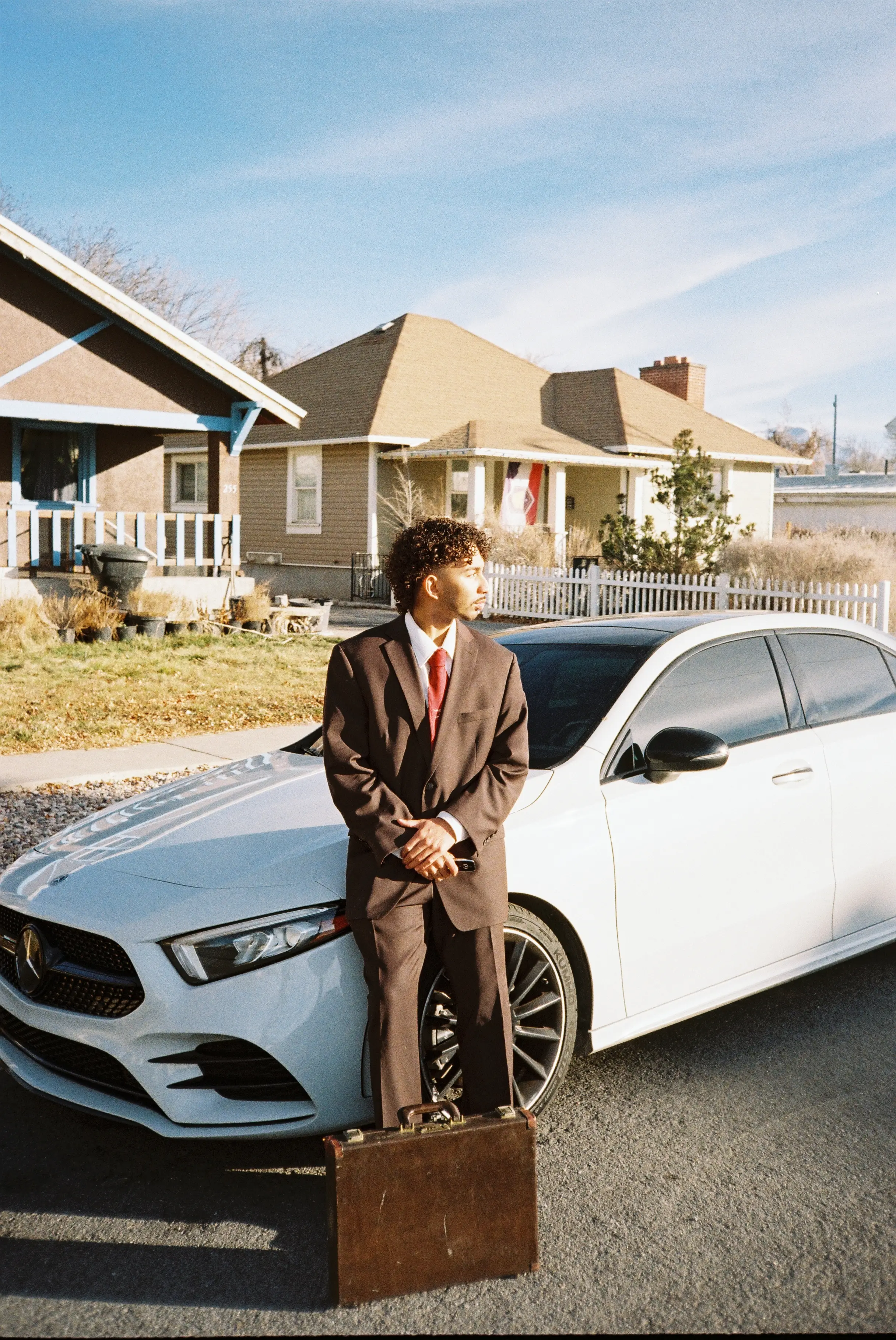 Joshua Barrera leaning on a white Mercedes in a brown suit